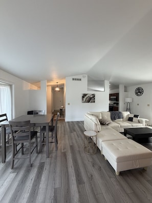 A modern living room with a dining area, a sofa set, and a kitchen in the background.