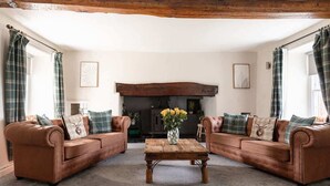 A living room with two brown leather sofas, a wooden coffee table, and plaid curtains. - 5-Bed North Wales Escape with Hot Tub & Views (Mochdre)