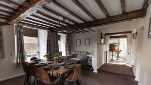 A dining area with a wooden table set for four, flanked by two chairs, a sofa, and a staircase leading to another room. - 5-Bed North Wales Escape with Hot Tub & Views (Mochdre)