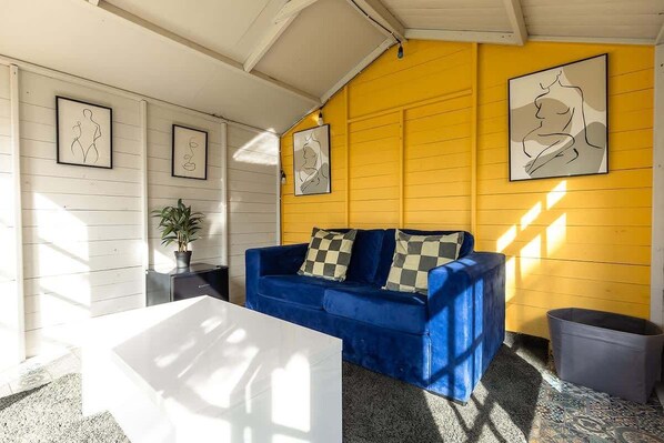 A room with a blue sofa, white walls, and a yellow accent wall. - 5-Bed North Wales Escape with Hot Tub & Views (Mochdre)