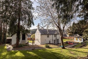 A stone house with a small attached shed, a swing set, and a well-maintained lawn. - 5-Bed North Wales Escape with Hot Tub & Views (Mochdre)