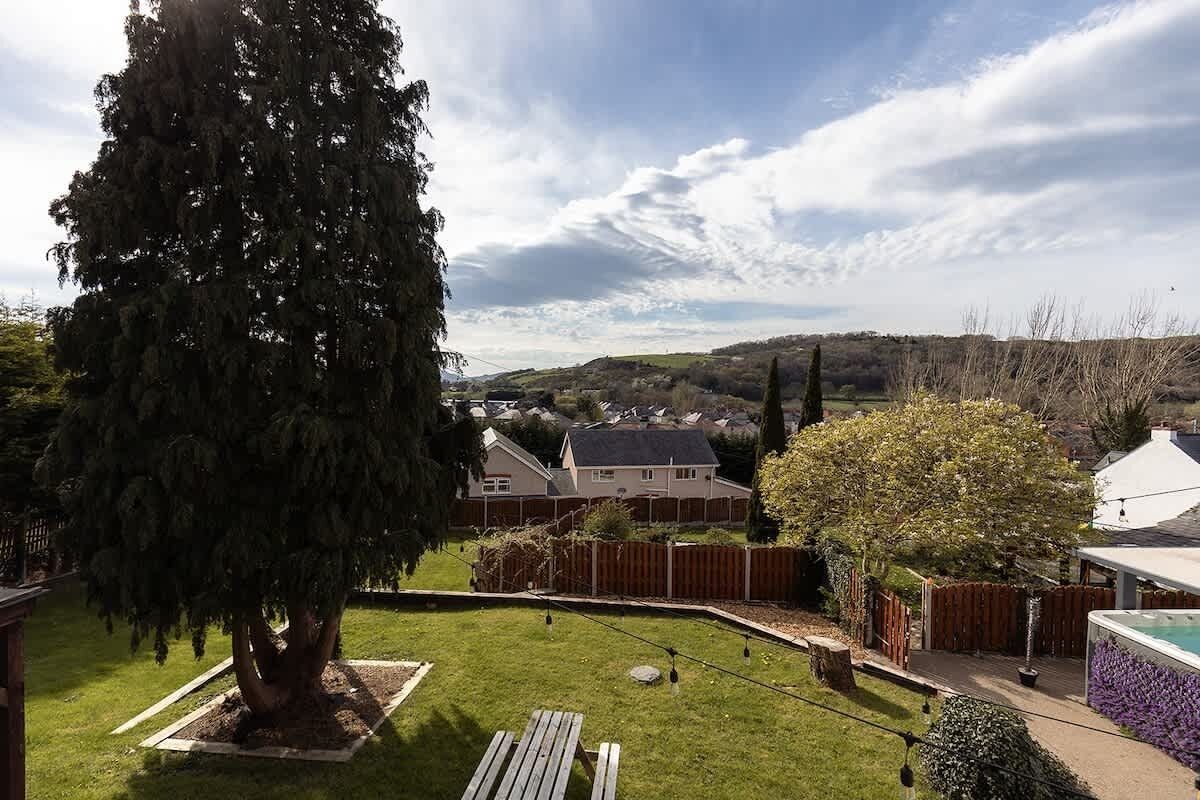 A residential backyard with a lawn, a wooden bench, a tree, and a swimming pool.