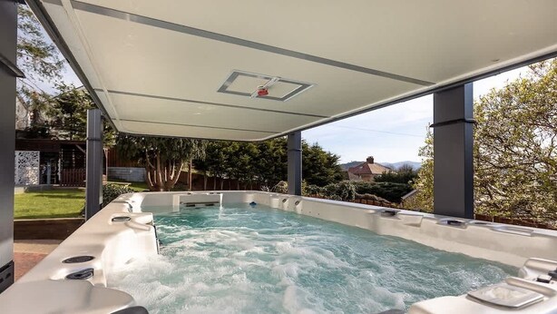 A hot tub with a glass enclosure, surrounded by a garden and trees. - 5-Bed North Wales Escape with Hot Tub & Views (Mochdre)