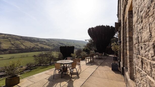 A patio with outdoor furniture, a stone wall, and a view of rolling hills.
