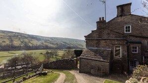 A stone building with a traditional design, a stone pathway leading to the entrance, and a view of rolling hills in the background.