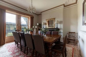 Ein Esszimmer mit Holztisch, Stühlen, einer Chandelieber, einem Spiegel und Blick durch große Fenster.