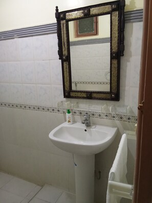 Ein Badezimmer mit einem weißen Waschbecken, einem Spiegel mit dekorativem Rahmen und einem Handtuchhalter.