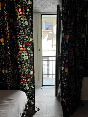 Ein Zimmer mit einem Bett, einer zur Außenseite führenden Tür und Vorhängen mit Obstmuster.