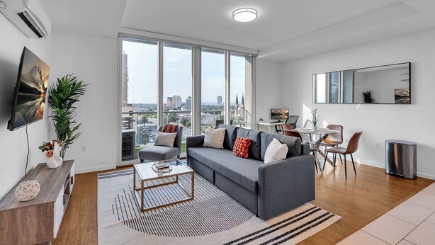 Ein modernes Wohnzimmer mit einem grauen Sofa, einem Couchtisch und einem Essbereich mit kleinem Tisch und Stühlen.