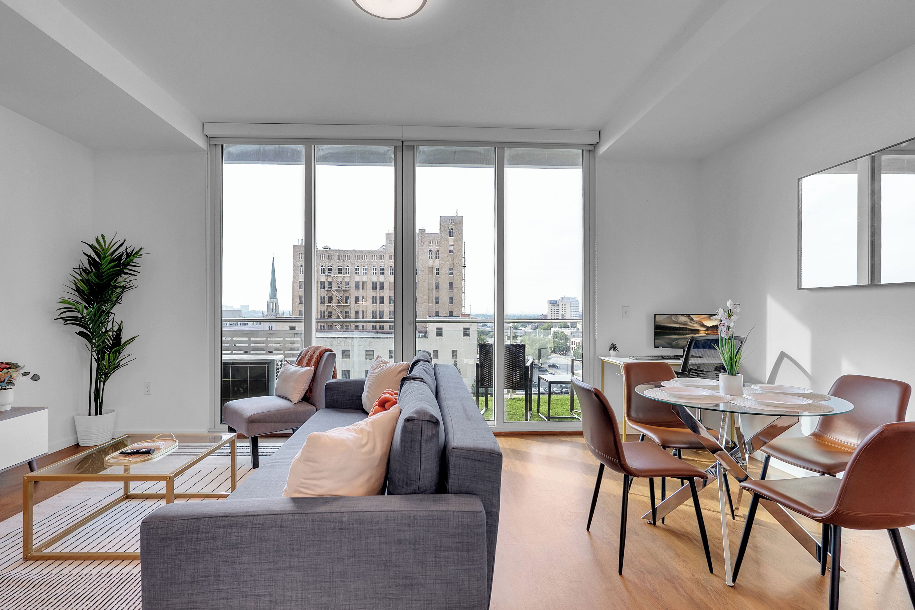 A modern living room with a grey sofa, a glass coffee table, and a dining area with a round table and chairs.