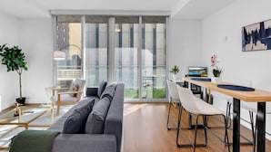 Ein modernes Wohnzimmer mit einer Couch, einem Esstisch mit Stühlen, einem Fernseher und einem großen Fenster mit Blick auf die Stadt.