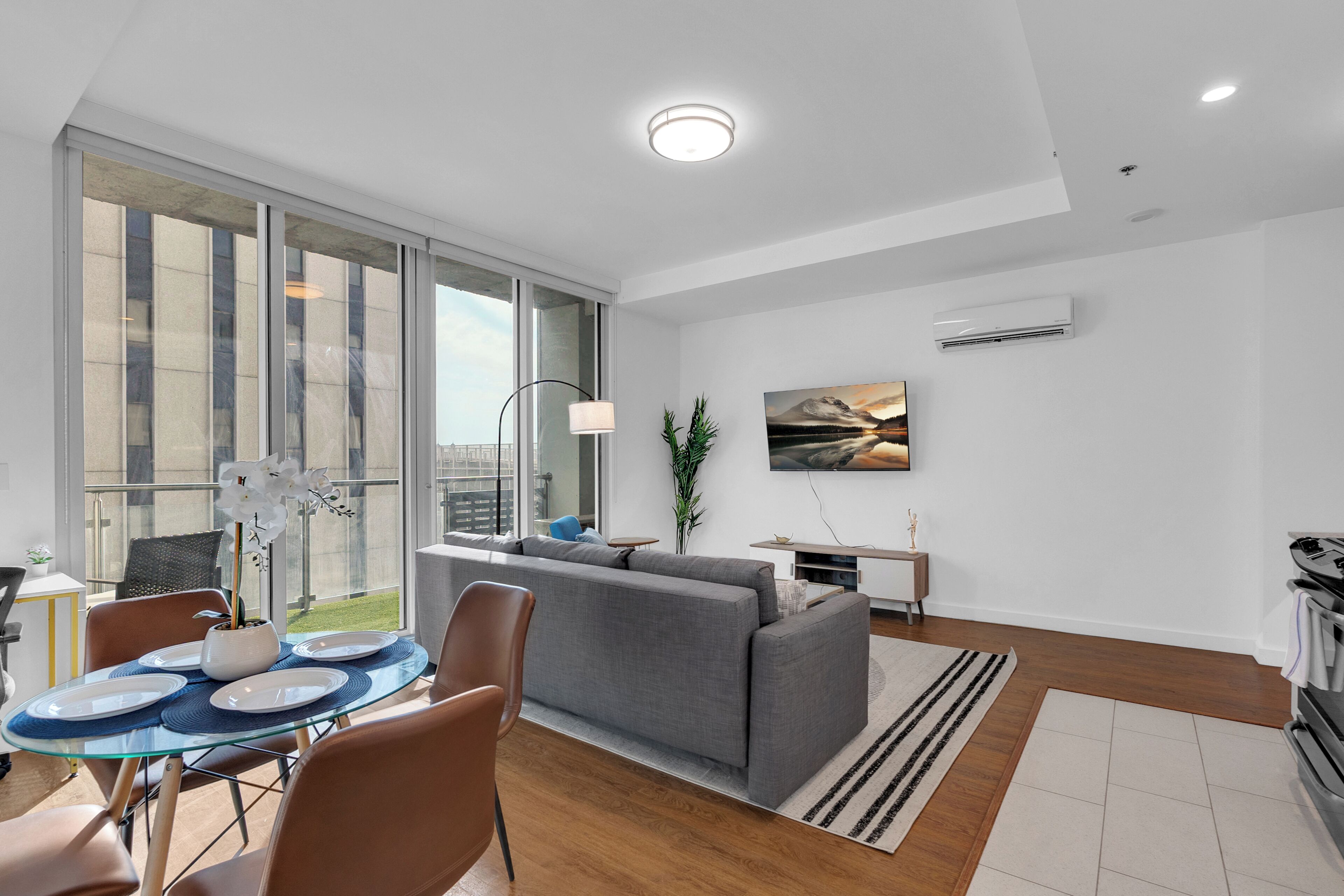 Ein modernes Wohnzimmer mit einem Glastisch, einem grauen Sofa und einem großen Fenster.