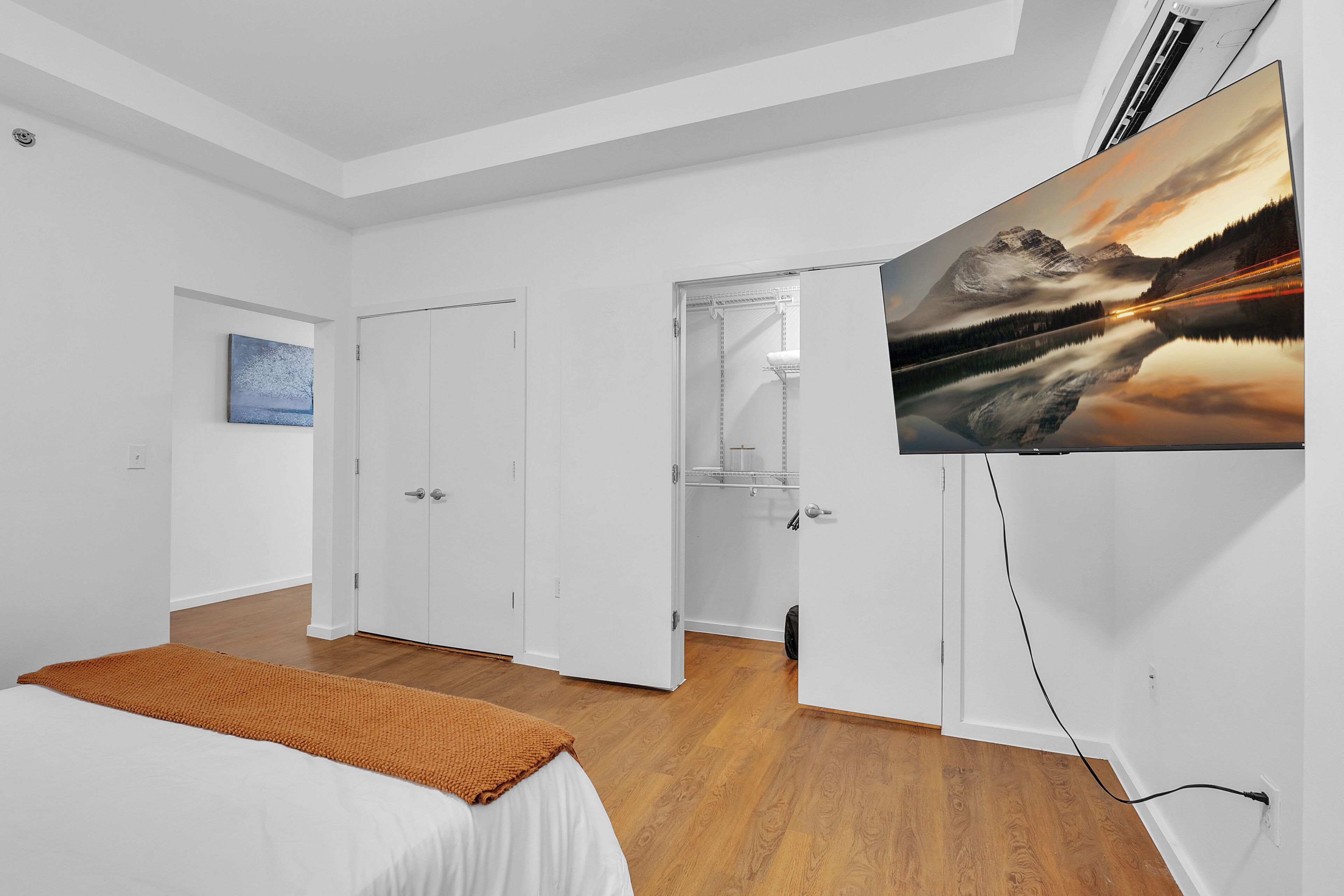 A bedroom with a bed, a TV mounted on the wall, and a door leading to another room.