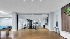 Ein geräumiger Raum mit Billardtisch, Fitnessgeräten und einem großen Fernseher an der Wand.