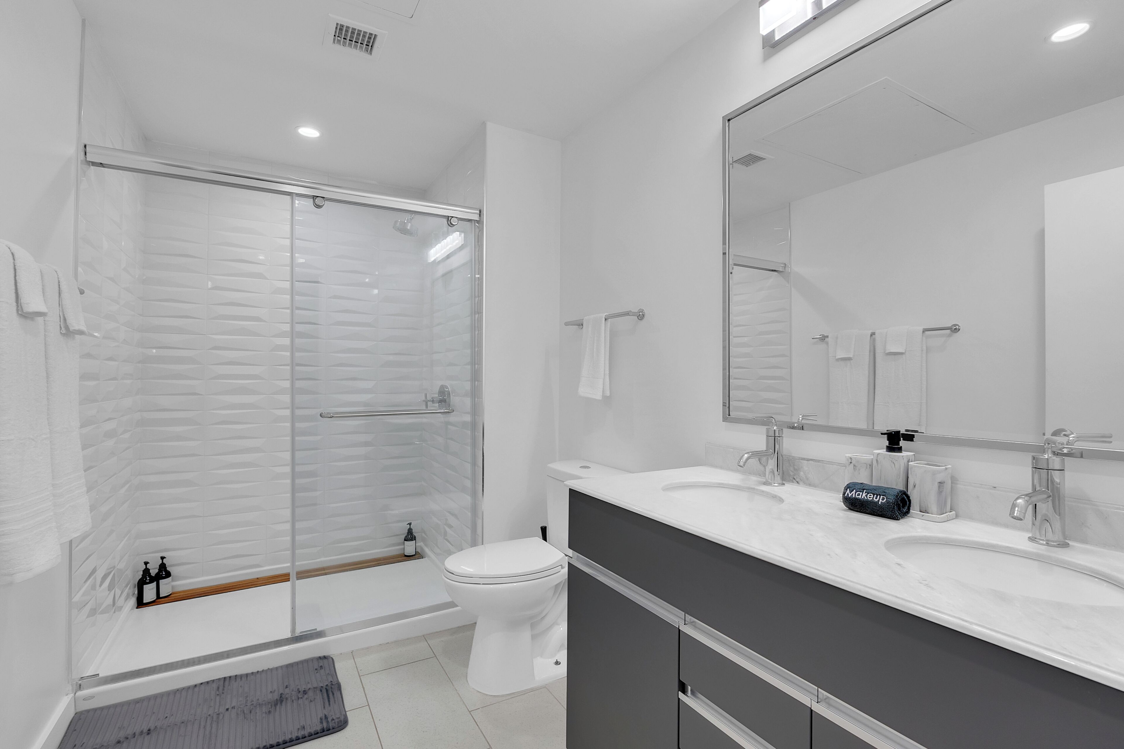 A modern bathroom with a glass-enclosed shower, a white toilet, and a vanity with a large mirror.