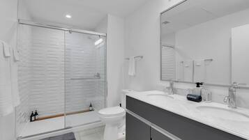 A modern bathroom with a glass-enclosed shower, a white toilet, and a vanity with a large mirror.