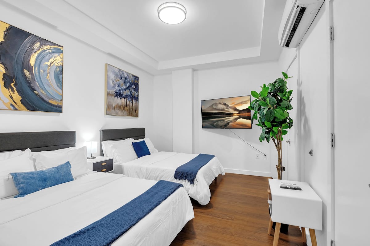 A hotel room with two beds, a TV, a plant, and artwork on the walls.