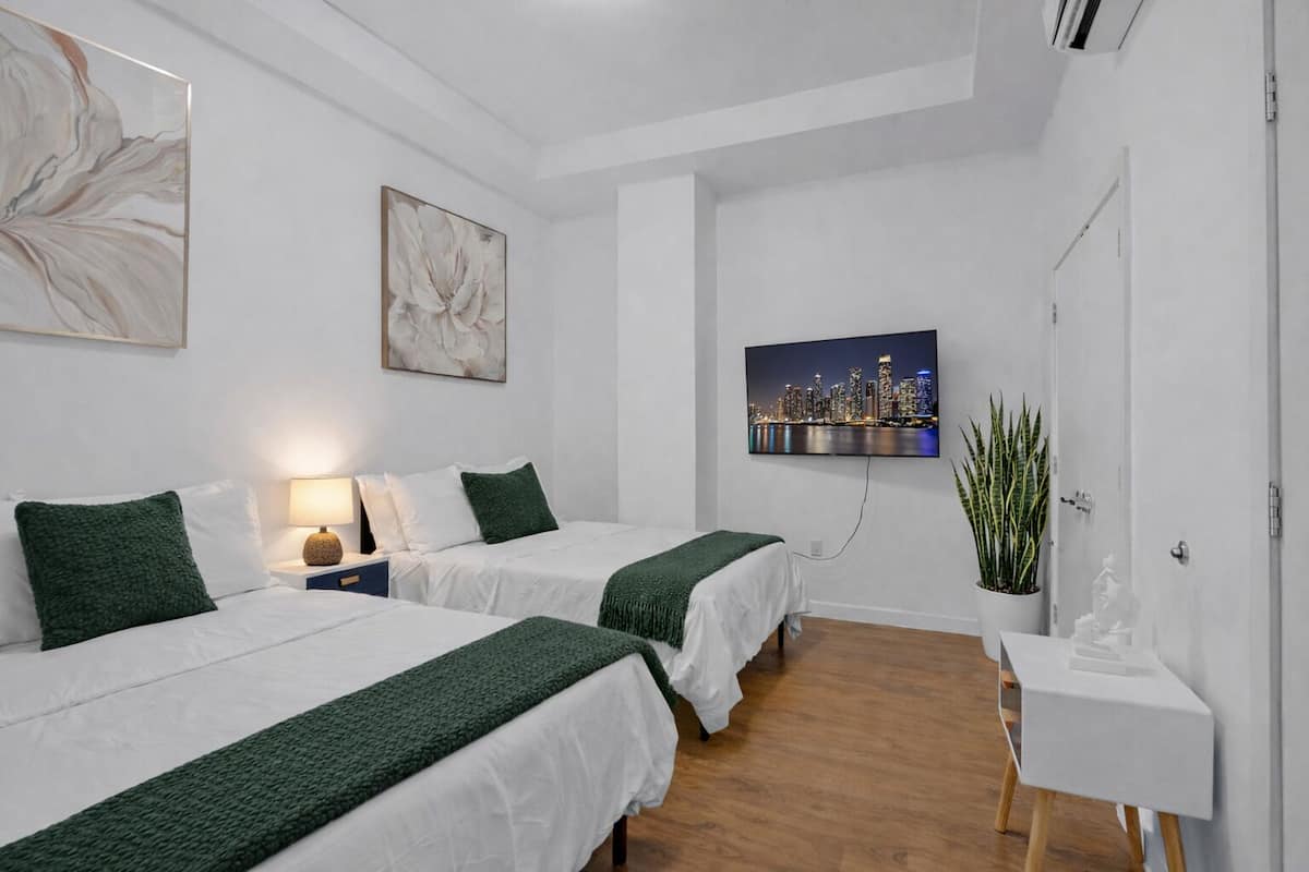 A hotel room with two beds, a TV, a plant, and artwork on the walls.