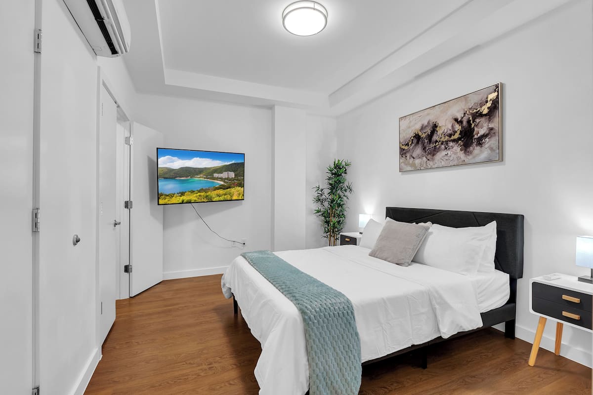 A modern bedroom with a bed, bedside table, wall-mounted TV, and artwork.