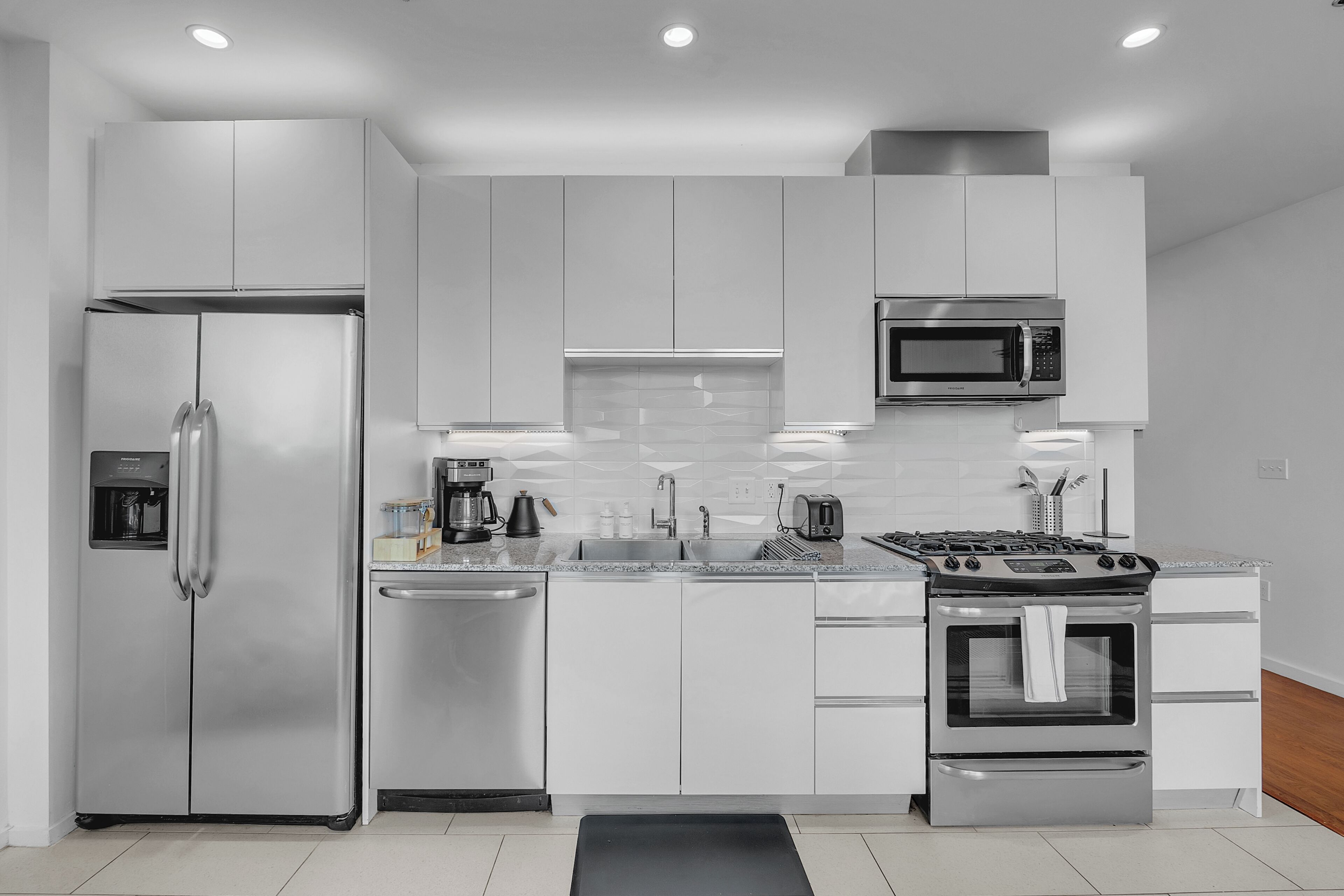 A modern kitchen with stainless steel appliances, white cabinetry, and a tiled backsplash.