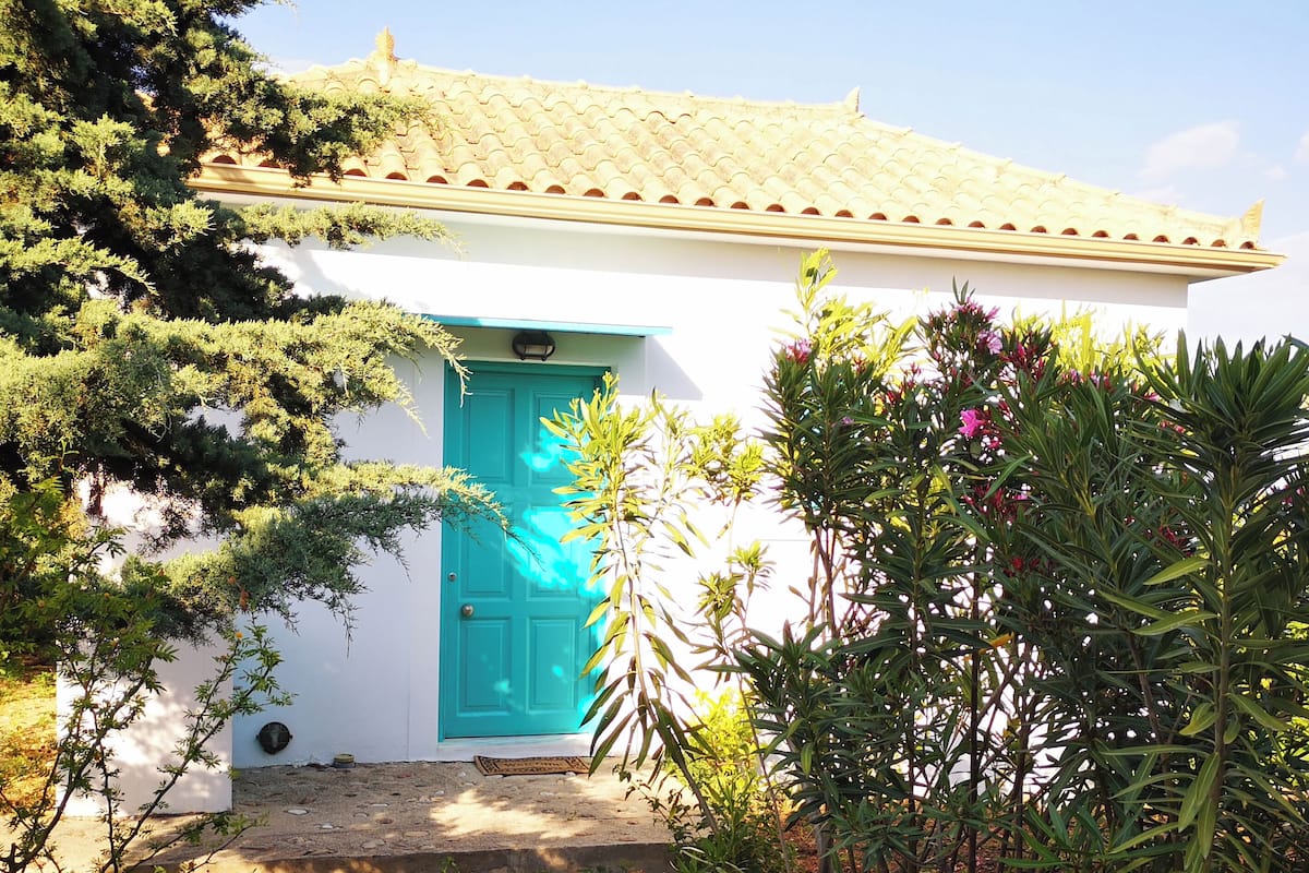 A small building with a turquoise door, surrounded by greenery.