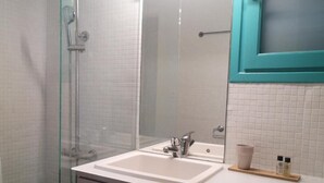 A bathroom with a glass shower enclosure, a white sink with a mirror, and a teal-framed medicine cabinet.