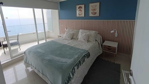 A bedroom with a bed, a nightstand, a lamp, a window with a view, and two framed pictures on the wall. - Apartment in Concon, in front of the sea. Wonderful view. 5 people, very complete. (Concón)