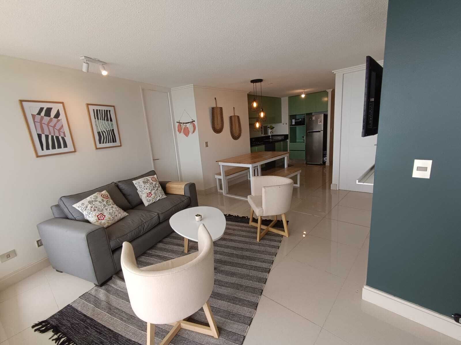 A modern living room with a sofa, two white chairs, a dining table, and a kitchen in the background.
