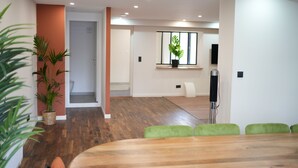 Een moderne hotelkamer met een houten vloer, groene bekleden stoelen, een kamerplant en een flatscreen-televisie.