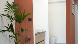 Een gang met een potplant, houten vloeren en een badkamer in de achtergrond.
