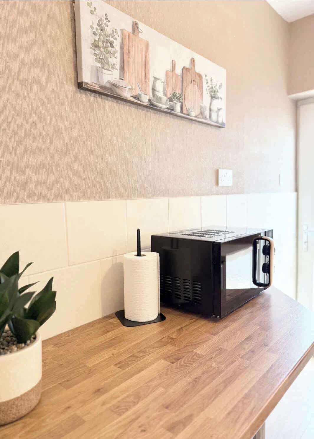 A kitchen counter with a microwave, a roll of paper towels, and a potted plant.