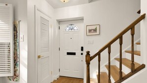 A hallway with a wooden staircase, a white door with a window, and a framed picture on the wall. - Your Old Town Home Away From Home (Alexandria)