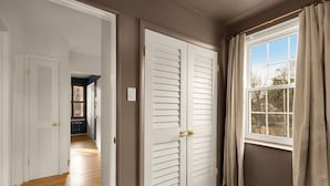 A hallway with a wooden floor, white doors, and a window with curtains. - Your Old Town Home Away From Home (Alexandria)