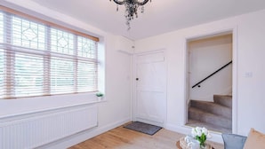 Ein Zimmer mit Heizkörper, einem Fenster mit Jalousien, einer Tür, einer Treppe, einem kleinen Tisch mit Tablett und einem Sofa.