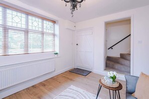 Ein Zimmer mit Heizkörper, einem Fenster mit Jalousien, einer Tür, einer Treppe, einem kleinen Tisch mit Tablett und einem Sofa.