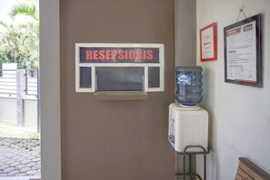 A reception area with a sign labeled 'RESEPSIONIS,' a water dispenser, and two framed documents on the wall. - Cozy Double Escape W/ Free WiFi and Parking (Banda Aceh)