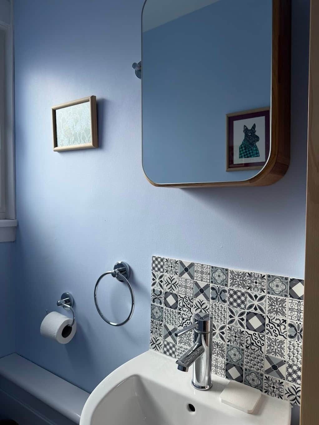 Une salle de bain avec un mur bleu, un lavabo blanc, un miroir, un porte-serviettes et des carreaux à motifs.