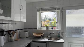 A kitchen with white cabinets, a window with a view of trees, a sink, and a dishwasher.
