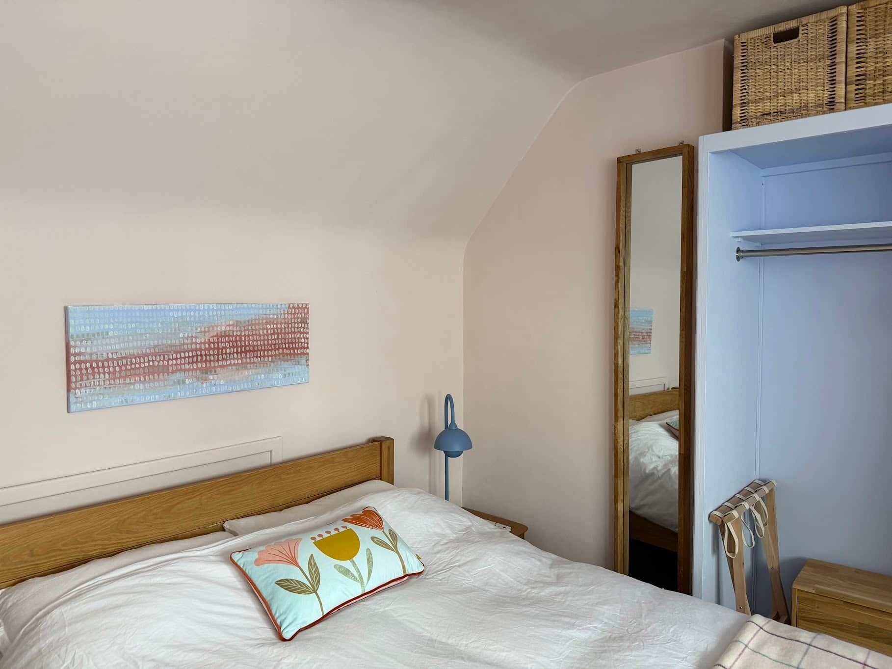 A bedroom with a bed, a nightstand, a lamp, a mirror, and a wall art piece.