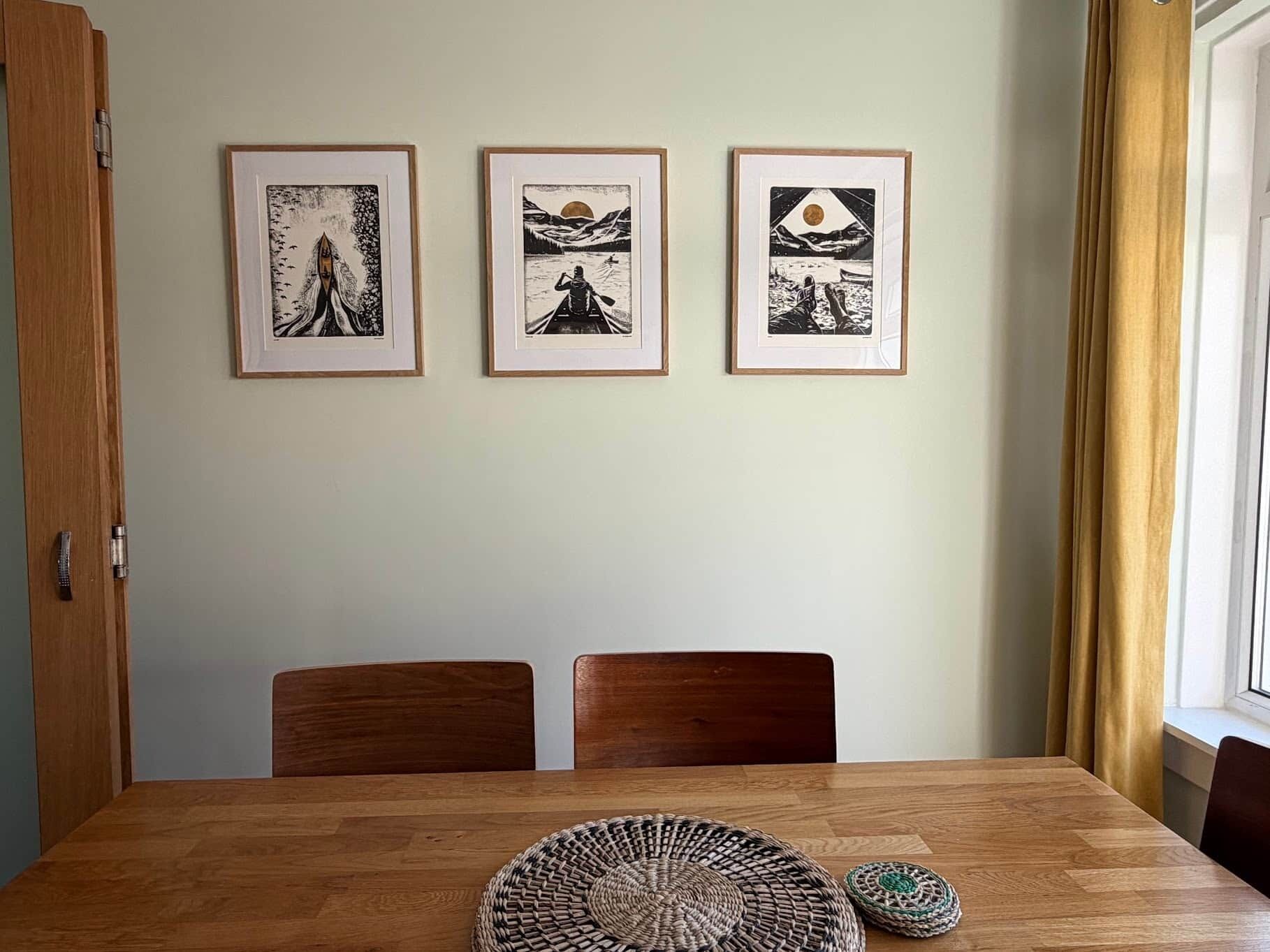 En matplats med ett träbord, tre inramade konstverk och två stolar.