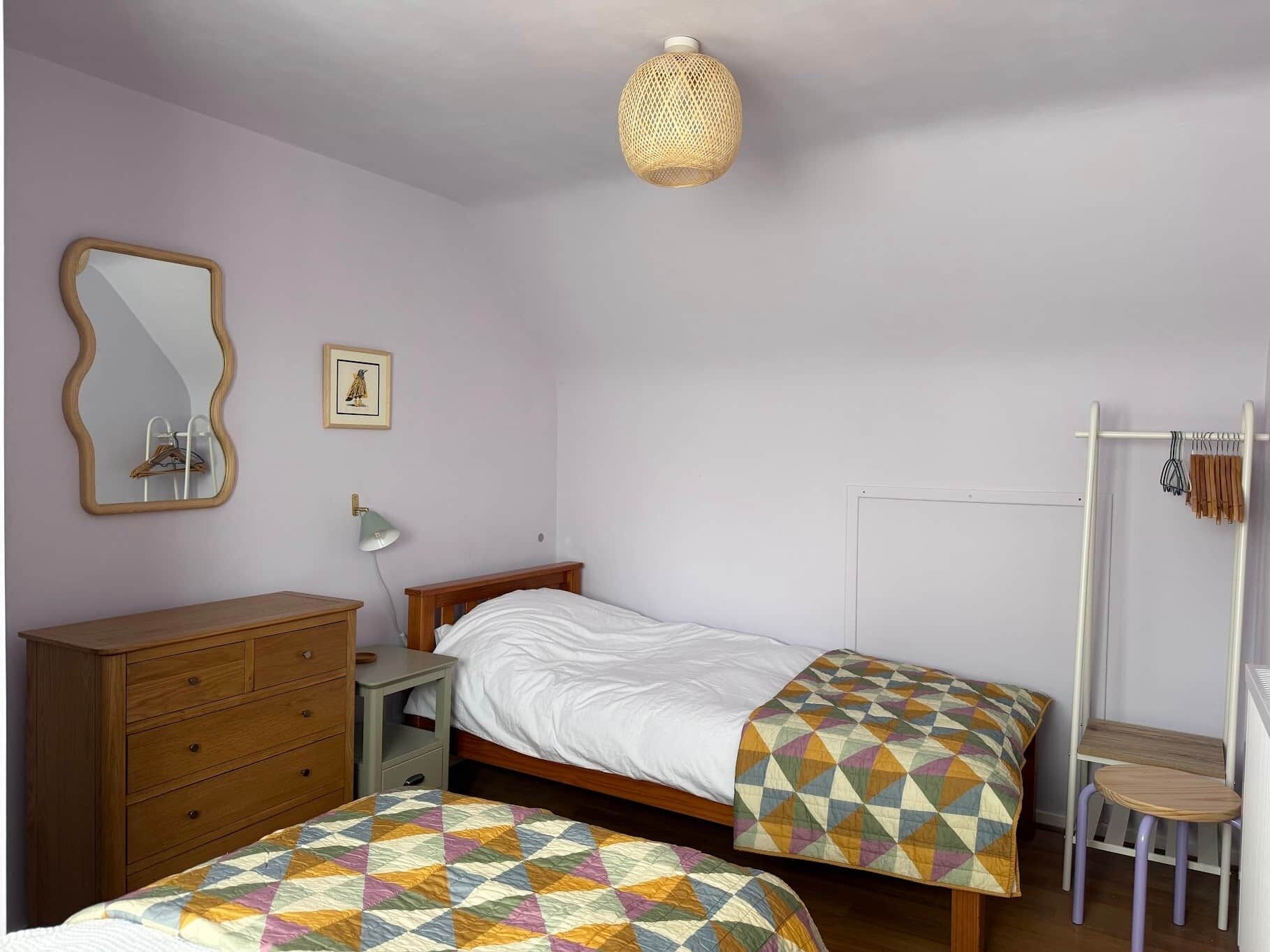 Un dormitorio con dos camas, un aparador, un espejo, una lámpara colgante y un armario.