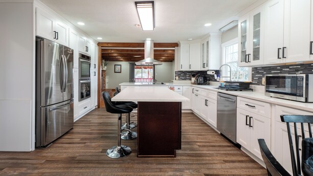 Una cocina moderna con armarios blancos, electrodomésticos de acero inoxidable, una isla central y techo de madera.