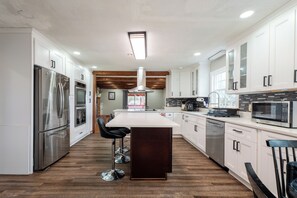 Une cuisine moderne avec des armoires blanches, des appareils en acier inoxydable, un îlot central et un plafond en bois.