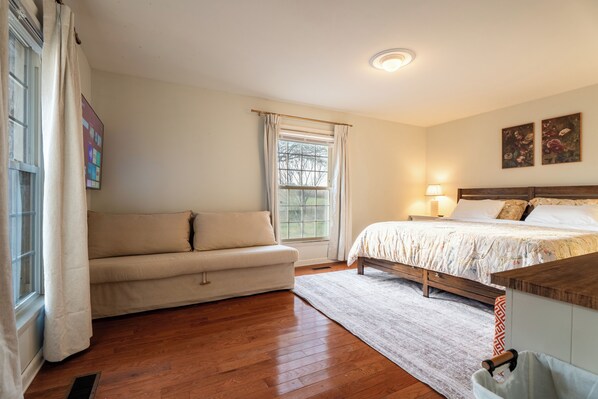 Une chambre à coucher avec un lit, un canapé, une fenêtre avec des rideaux et une table de chevet avec une lampe.