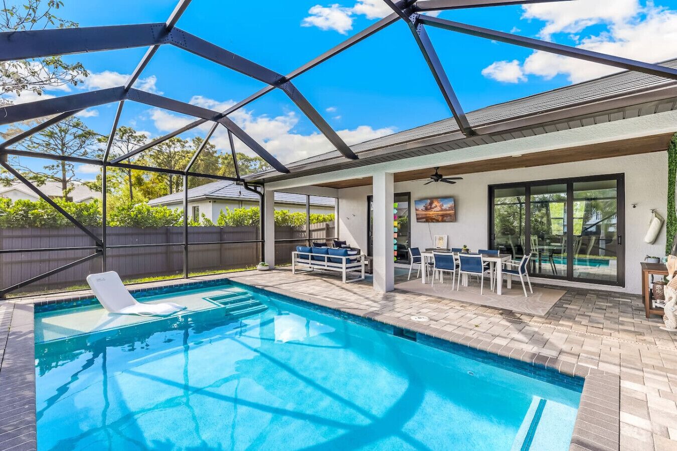 A covered outdoor swimming pool with a patio area, seating, and a ceiling fan.