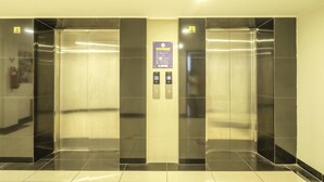 Um elevador com dois botões, uma placa com instruções de emergência e um indicador de andar.