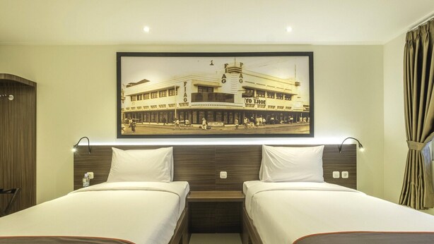 Quarto de hotel com duas camas, uma moldura grande com uma fotografia na parede e uma cabeceira de madeira.