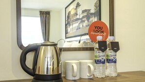 Quarto de hotel com chaleira, duas canecas brancas, duas garrafas de água e um letreiro com a mensagem 'Você está incrível'.