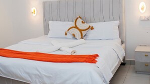 Ein ordentlich bezogenes Bett mit weißen Leinen, einem Zierkissen und einer orangefarbenen Tagesdecke.