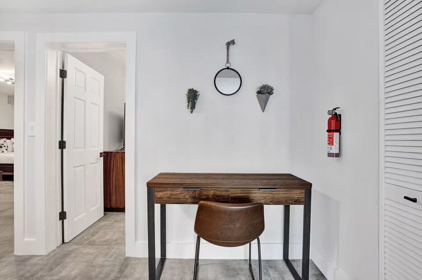 Una habitación con una mesa de madera, una silla, un espejo y un extintor de incendios en la pared.